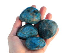 Four large blue apatite tumbled crystals on hand with white background