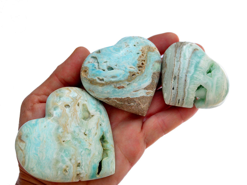 Three blue aragonite crystal hearts on hand with white background