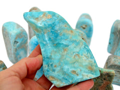 One large blue aragonite free form crystal 100mm on hand with background with some stones on white