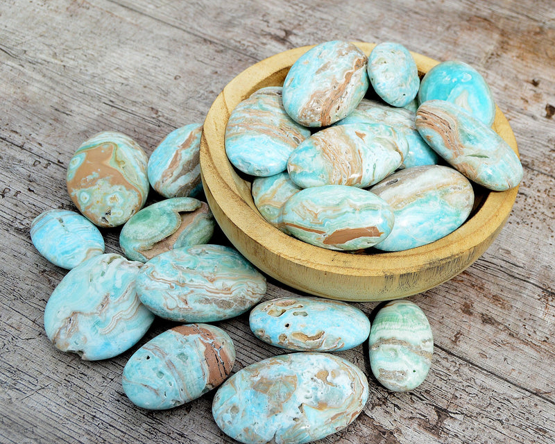 Several blue aragonite palm stones inside a wood bowl on wood table with another palmstones
