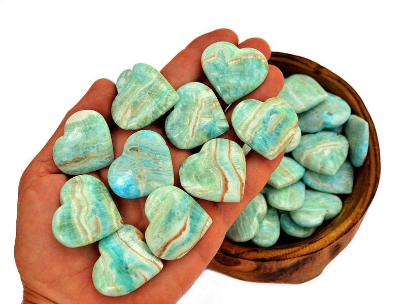 Ten blue aragonite hearts 30mm-35mm on hand with background with some hearts inside a wood bowl on white