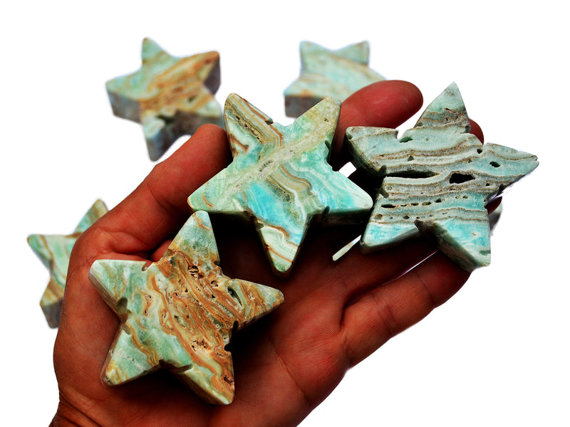 Three blue aragonite stars 60mm on hand with background with some crystals on white