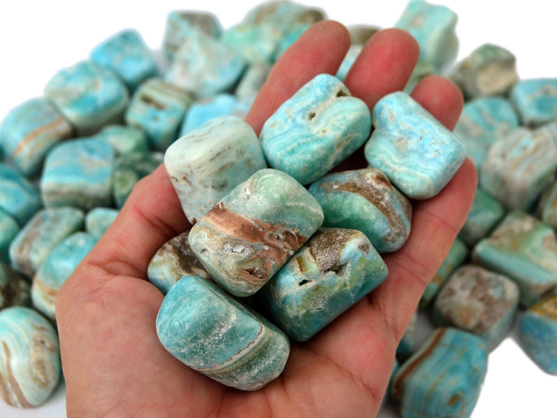 Some blue aragonite mini tumbled stones on hand with background with several crystals on white