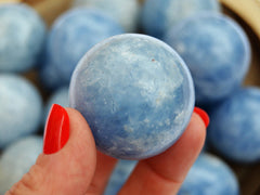 One blue calcite sphere stone 45mm on hand with background with some spheres inside a wood bowl