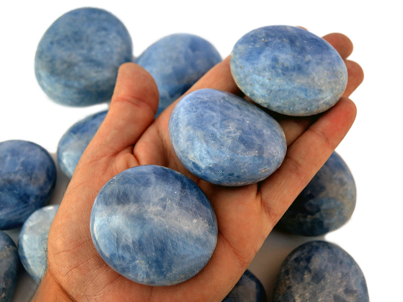 Three blue calcite palm stones 40mm-70mm on hand with background with some crystals on white