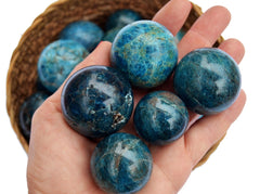 Some blue apatite crystal spheres 25mm-40mm on hand with background with some crystals inside a basket