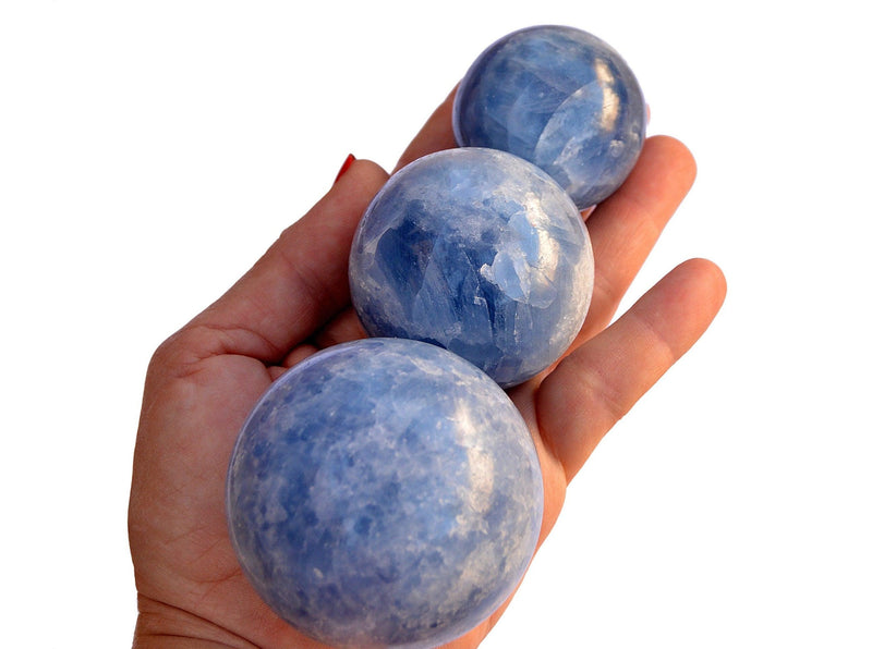Three blue calcite sphere crystals 40mm-60mm on hand with white background