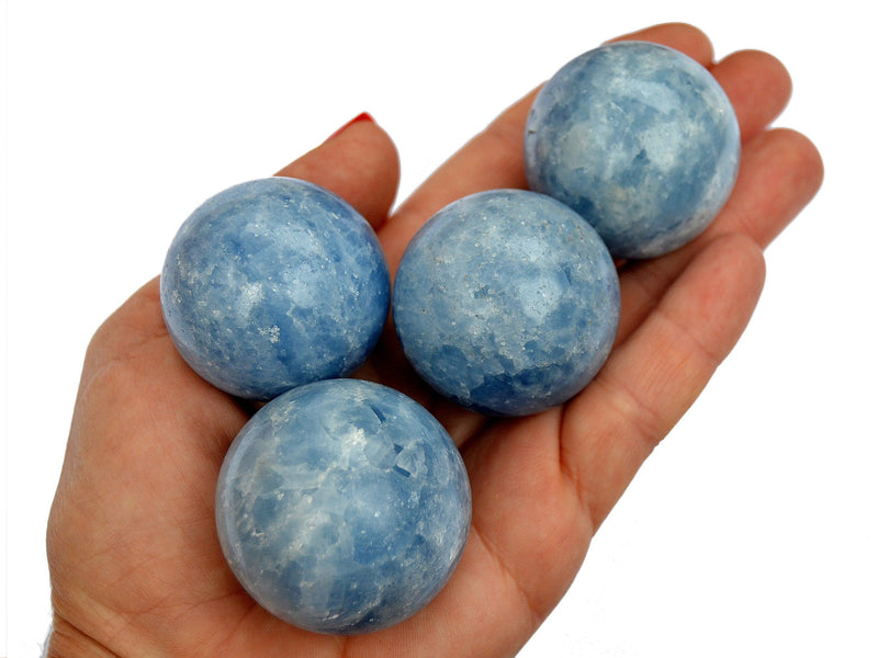 Four blue calcite spheres 35mm-40mm on hand with white background