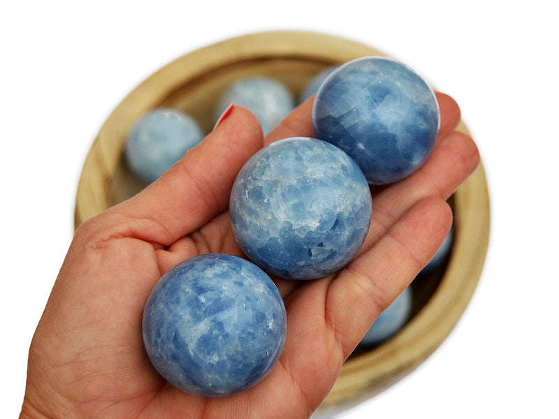 Three blue calcite sphere crystals 25mm-40mm on hand with background with some balls inside a wood bowl
