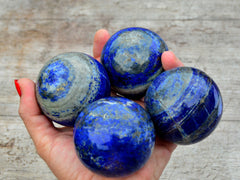 Three blue lapis lazuli sphere crystals 50mm-60mm on hand with wood background