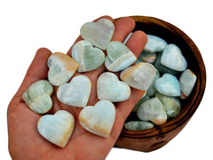Ten blue green caribbean calcite crystal hearts 25mm-30mm on hand with background with some hearts inside a wood bowl on white
