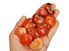 Ten small carnelian heart crystals 30mm on hand with white background