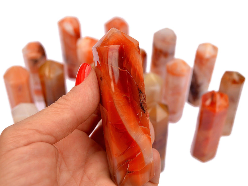 One carnelian crystal tower 90mm on hand with background with some obelisks on white