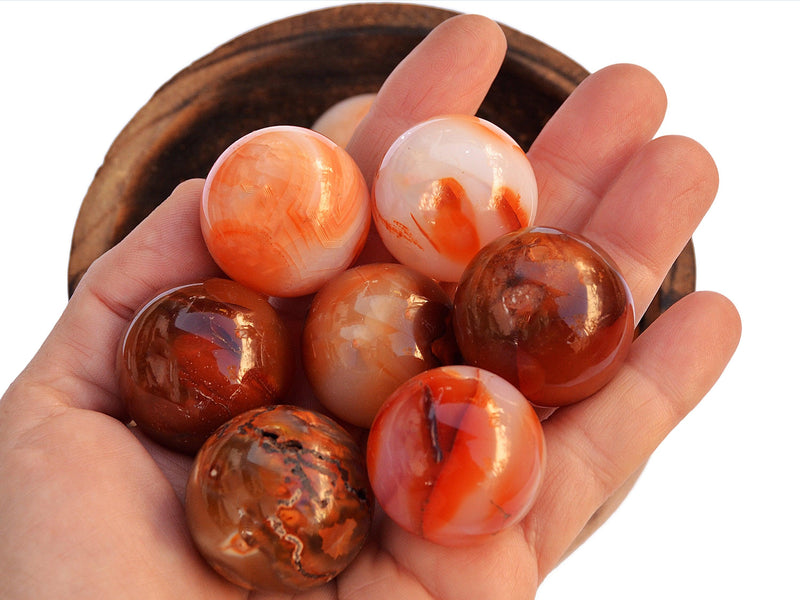 Seven carnelian crystal spheres 55mm-60mm on hand with background with some spheres inside a wood bowl on white