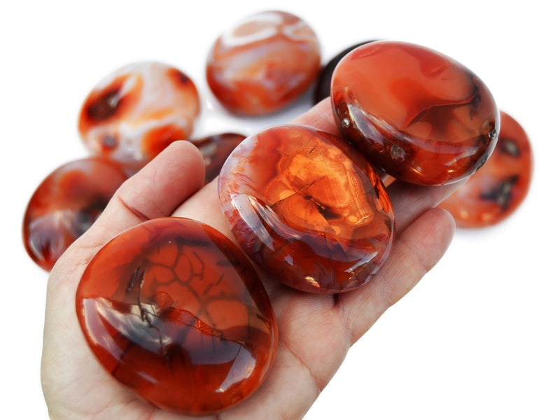 Three carnelian palm stones 40mm-70mm on hand with background with some stones on white