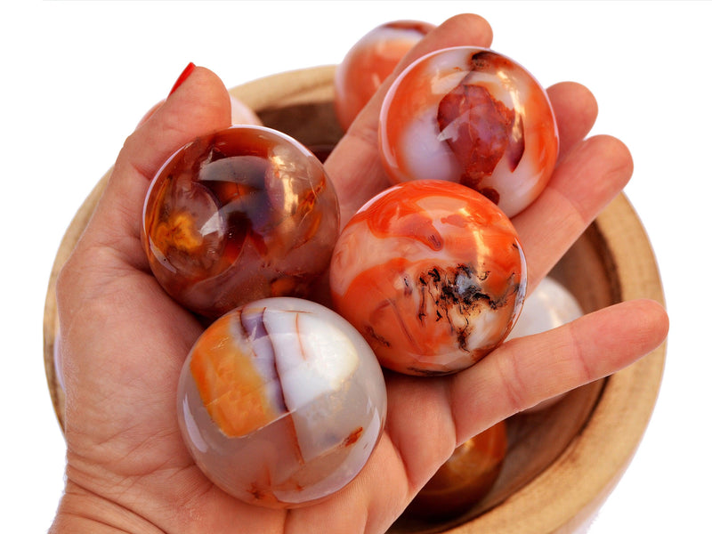 Four carnelian crystal spheres 55mm-60mm on hand with background with some spheres inside a wood bowl on white