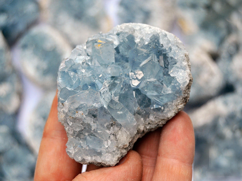 Blue celestite crystal cluster 50mm on hand with background with some crystals 