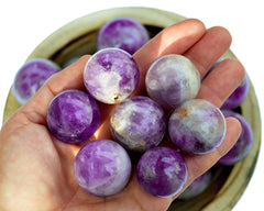 Some amethyst crystal spheres 25mm - 40mm on hand with background with some crystals inside a bowl
