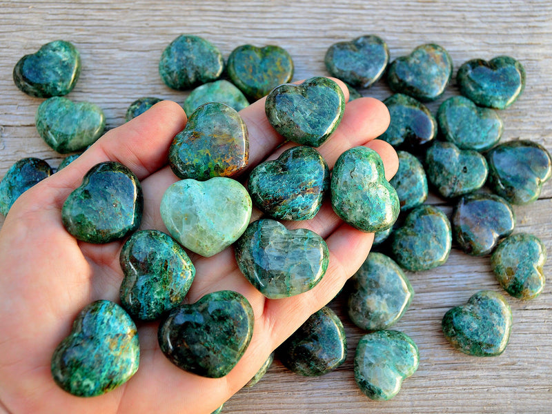 Ten green chrysocolla crystal hearts 30mm on hand with background with some crystals on wood table