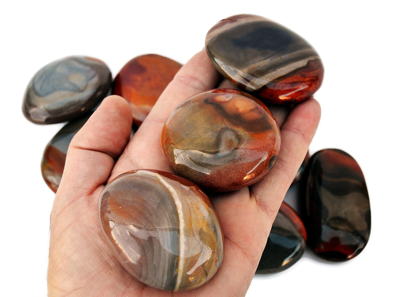 Three polychrome jasper palm stones 70mm-40mm on hand with background with some crystals