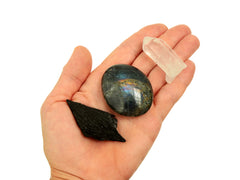 Raw black kyanite, labradorite palm stone and raw clear quartz point on hand with white background