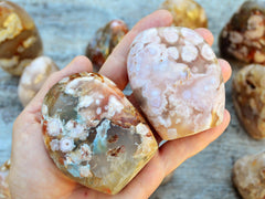 Two flower agate free forms on hand with background with some crystals on wood table