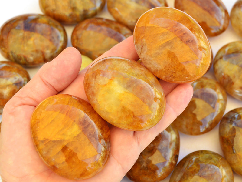 Three yellow hematoid quartz palm stones 60mm-65mm on hand with background with several crystals on white