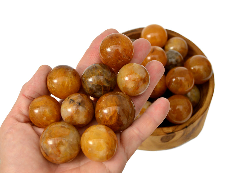 Some golden healer quartz spheres 25mm-40mm on hand and some crystals inside a wood bowl on white background