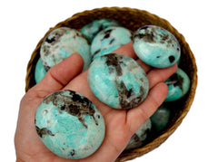 Three amazonite palm stones 40mm-60mm on hand with background with some stones inside a basket