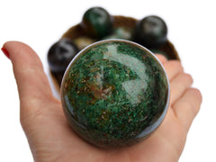 One green chrysocolla sphere 60mm on hand with background with some crystals inside a straw basket on white