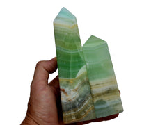 Two large green pistachio calcite crystal obelisks on hand with white background