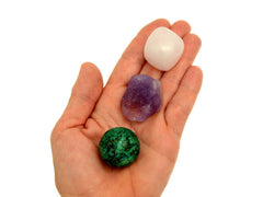 One small tumbled mangano calcite, raw amethyst and chrycolla sphere on hand with white background 
