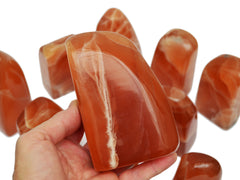 Honey calcite fre form crystal 110mm on hand with background with some stones on white