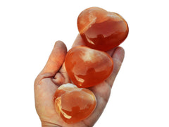 Three honey calcite crystal hearts 40mm-75mm on hand with white background