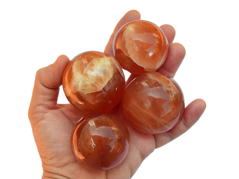 Four honey calcite crystal spheres 45mm-55mm on hand with white background