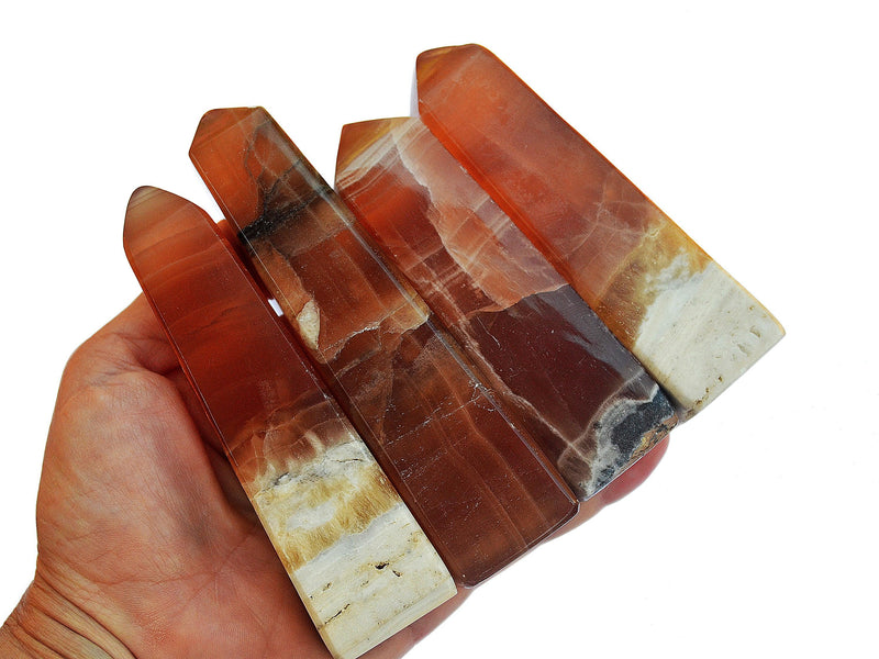 Four large honey calcite crystal towers on hand with white background