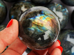 One rainbow labradorite sphere stone 60mm on hand with background with some balls
