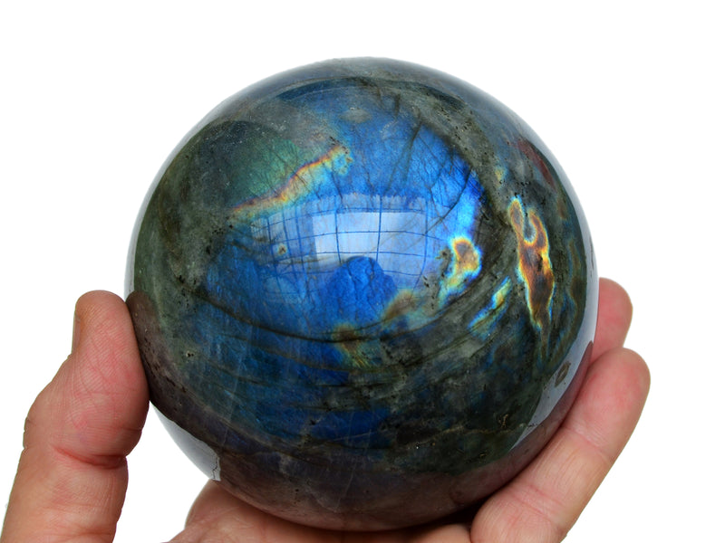 One large labradorite crystal sphere 90mm on hand with white background