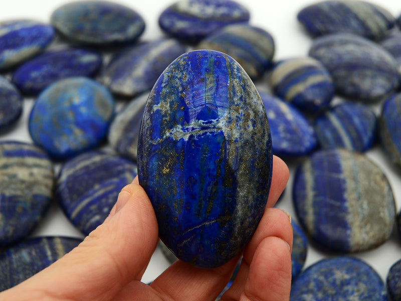 One lapis lazuli palm stone 70mm on hand with background with some stones on white