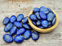Several lapis lazuli palm stones inside a wood bowl on wood table with some crystals with some rystals