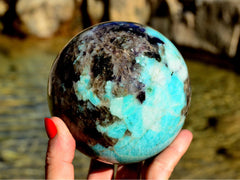 One extralarge green amazonite sphere 100mm on hand with background with river landscape