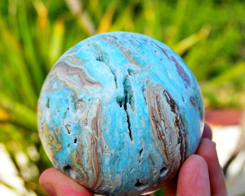 Blue large aragonite sphere on hand with background with green plants