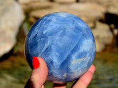 Large blue calcite sphere 100mm on hand with river landscape