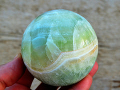 Large green pistachio calcite sphere 70mm on hand with wood background
