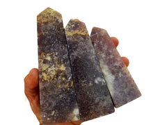 Three large purple lepidolite crystal towers on hand with white background