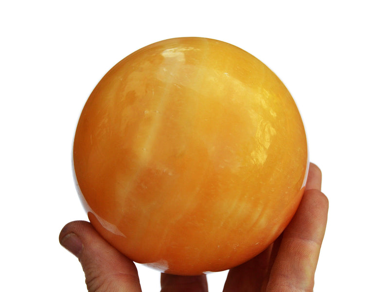 One large orange calcite sphere 85mm on hand with white background