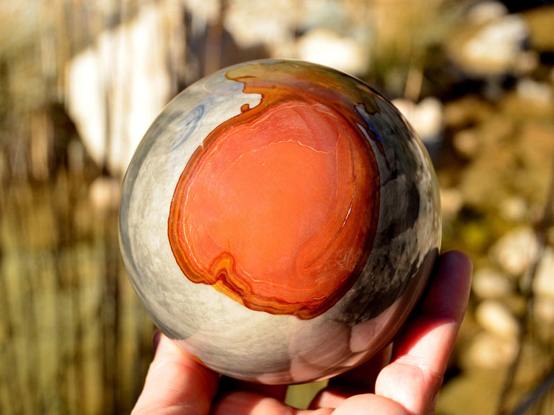 Large desert jasper sphere mineral 95mm on hand with nature background