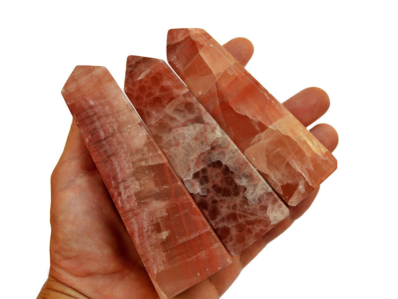 Three large rose calcite obelisks 100mm on hand with white background
