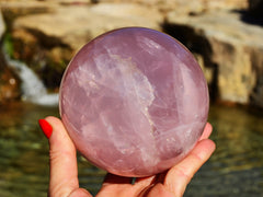 One large rose quartz sphere crystal 90mm on hand with background river landscape