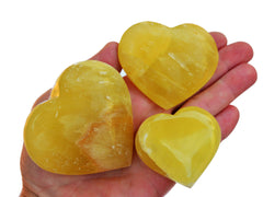 Three lemon yellow calcite heart crystals 50mm-75mm on hand with white background